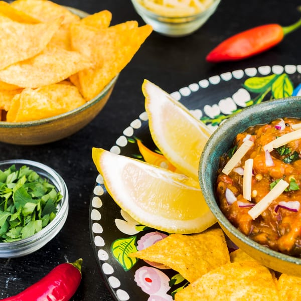 Mexican salsa with cheese, red onions, and lemon wedges, served with tortilla chips and cilantro.