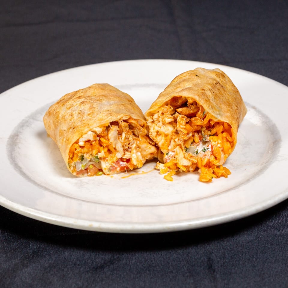 Two cut-open chicken and rice burritos filled with vegetables and sauce on a white plate.