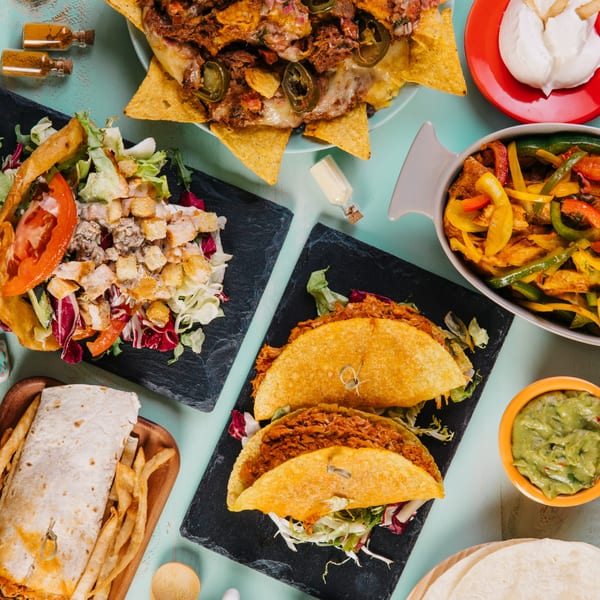 Overhead view of a Mexican feast including nachos, tacos, fajitas, burrito, salad, and guacamole.