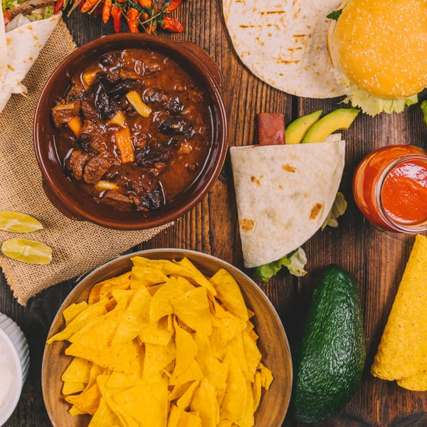 A top-down view of various Mexican dishes, including a stew, burritos, nachos, and a burger.