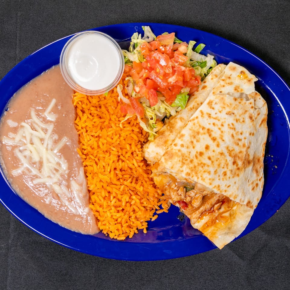 Mexican-style platter with a grilled chicken quesadilla, orange rice, refried beans, salad with pico de gallo, and sour cream.