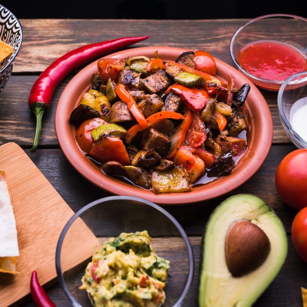 A vibrant platter of grilled vegetables, with guacamole, salsa, and tortilla chips on a wooden table.